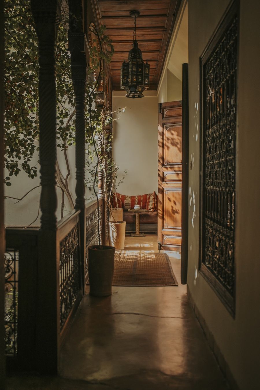 Coursive couverte du riad, lanterne suspendue et banquette kilim dans la pénombre