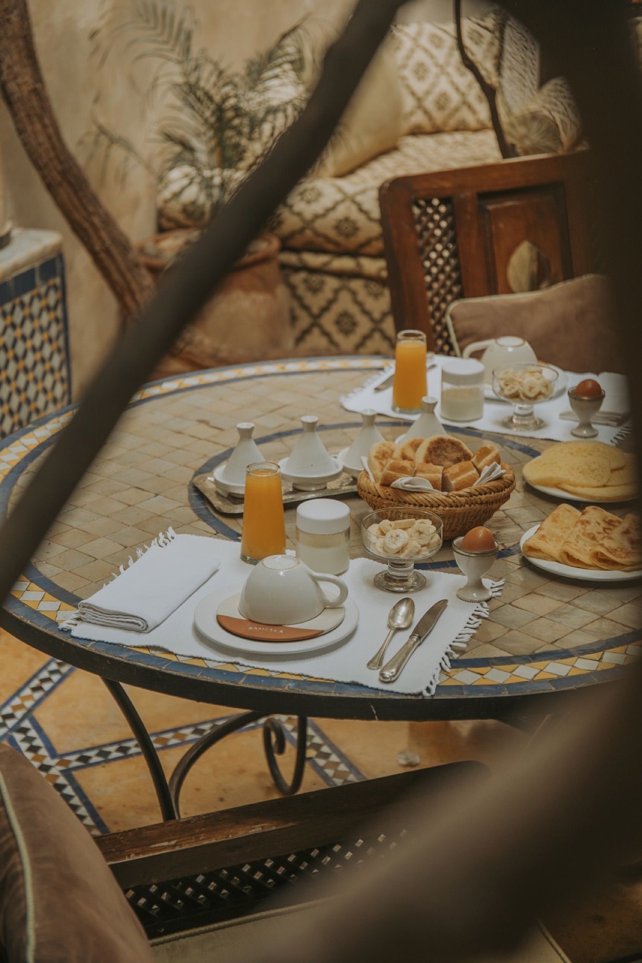 Petit-déjeuner marocain vu de haut sur une table en mosaïque : tajines, pains et jus d'orange