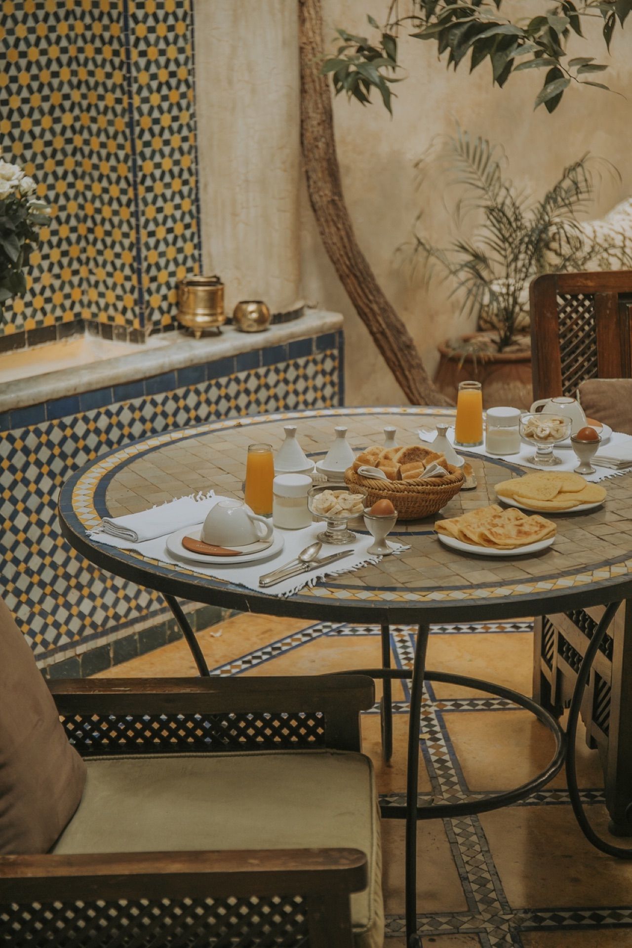 Table du petit-déjeuner dressée au patio, mur de zellige bleu et roses